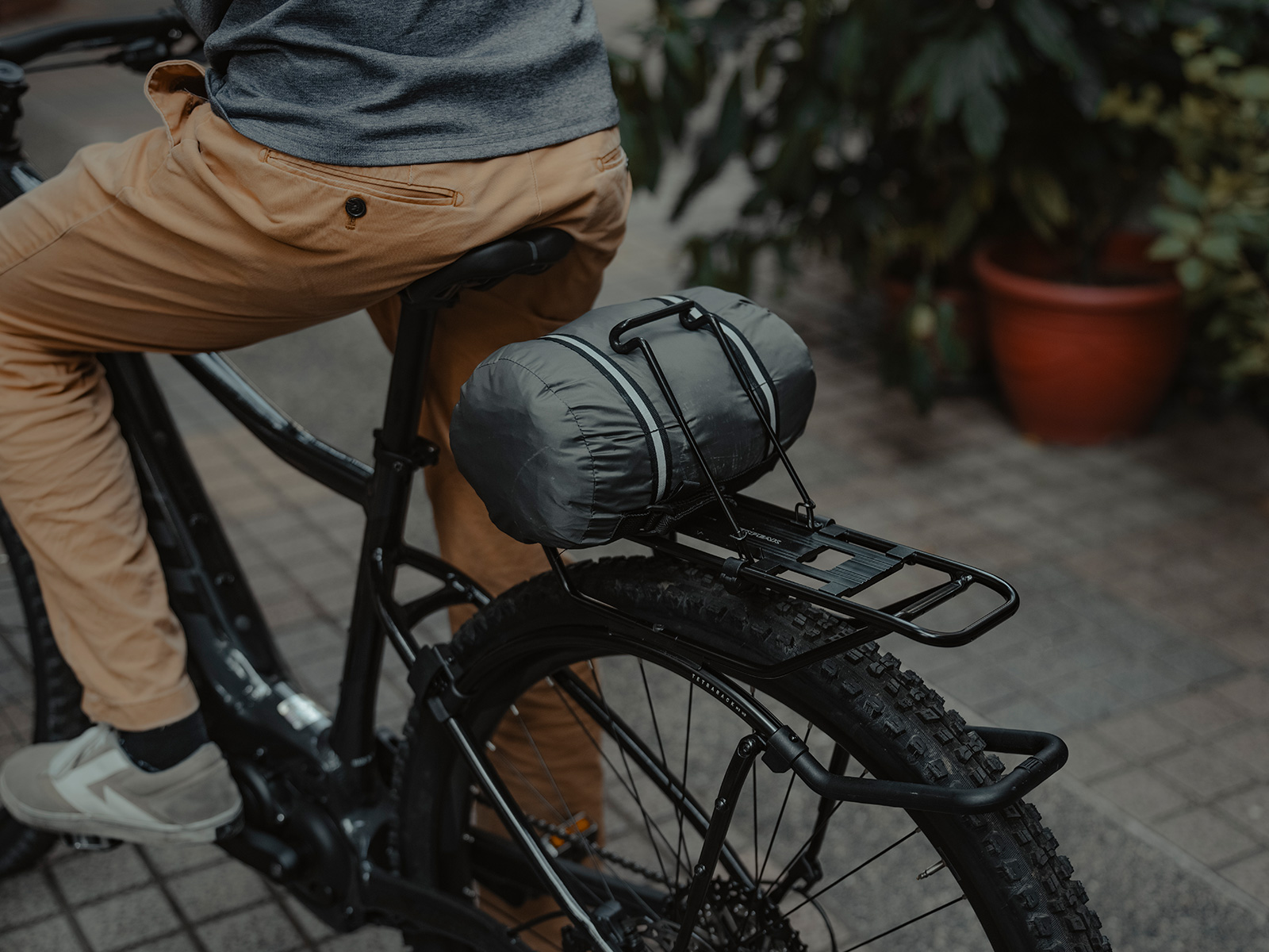 Topeak TetraRack Federklappe in Schwarz, montiert am Gepäckträger und fixiert eine graue Packtasche am E-Bike.