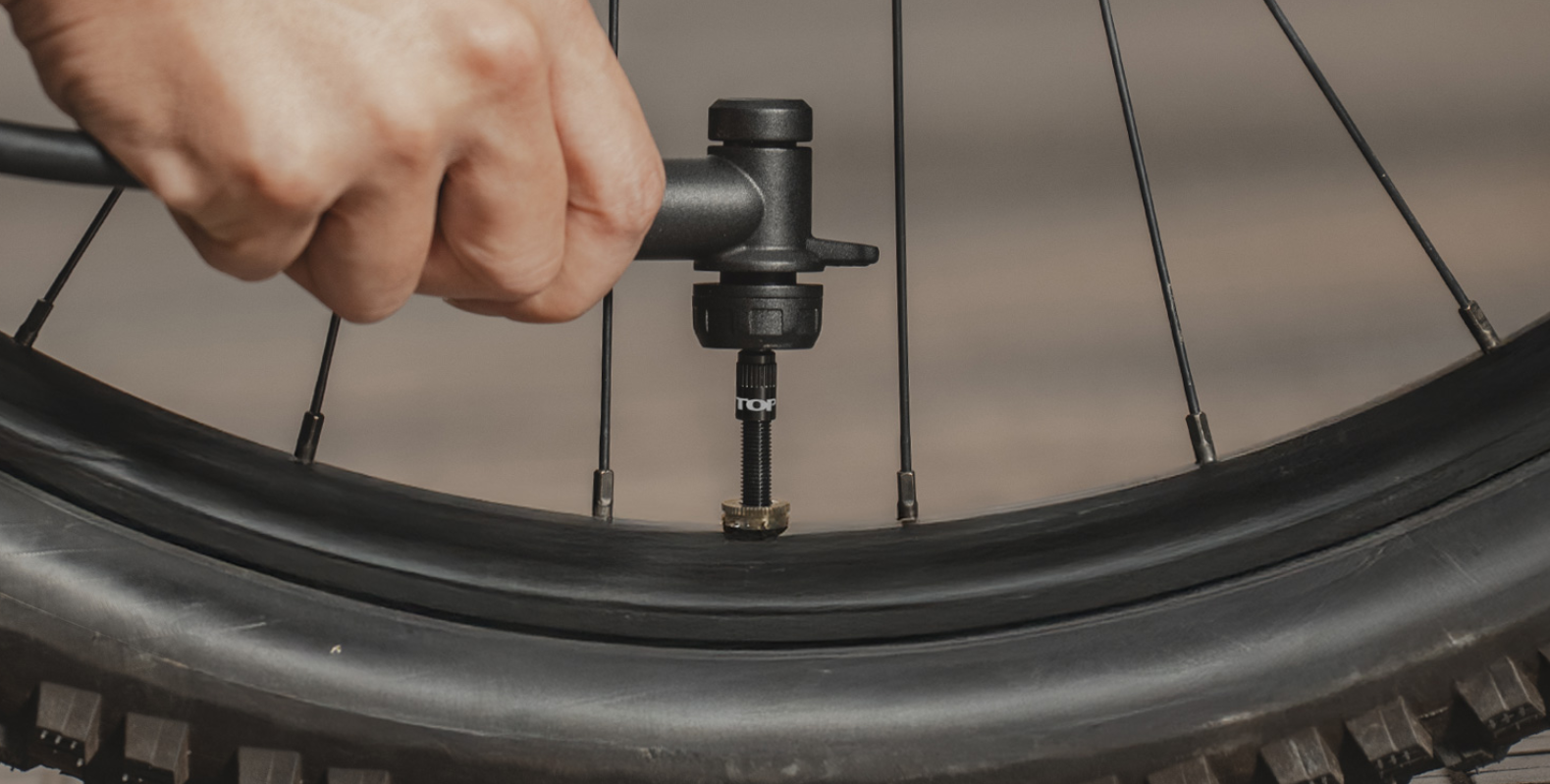  Tubeless-Ventil montiert in einem Mountainbike-Laufrad mit grobem Reifenprofil, im Outdoor-Einsatz auf einem Trail mit Pumpenkopf, teilweise verschmutzt.