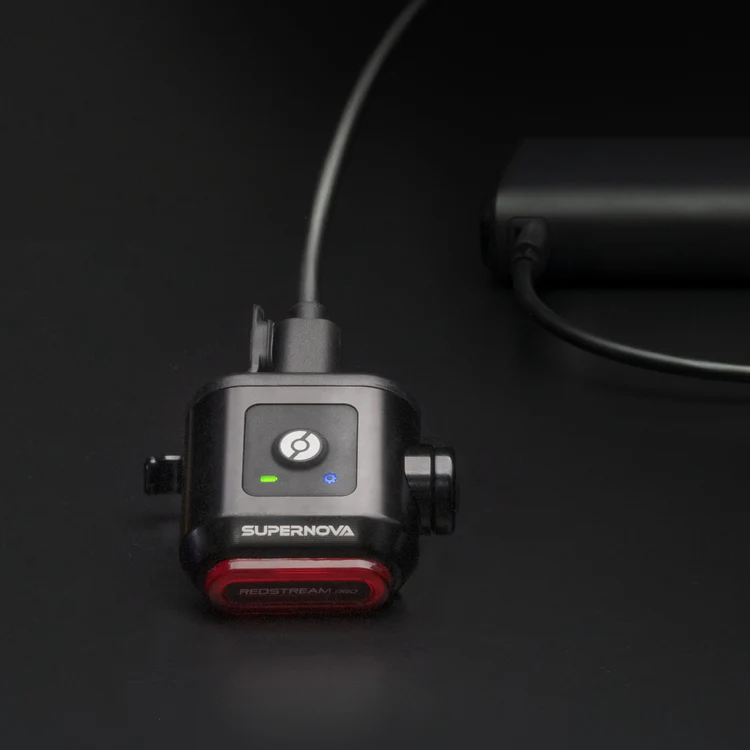  Supernova Redstream Pro Ruecklicht in Schwarz waehrend dem Laden mit USB-Kabel und Statusanzeige.