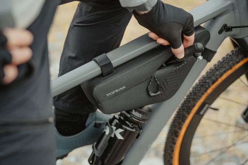 Livestylebild mit Topeak MidLoader Drybag in Grösse S in schwarz, montiert an einem Fahrrad, eine Männerhand entnimmt eine Pumpe aus der Tasche