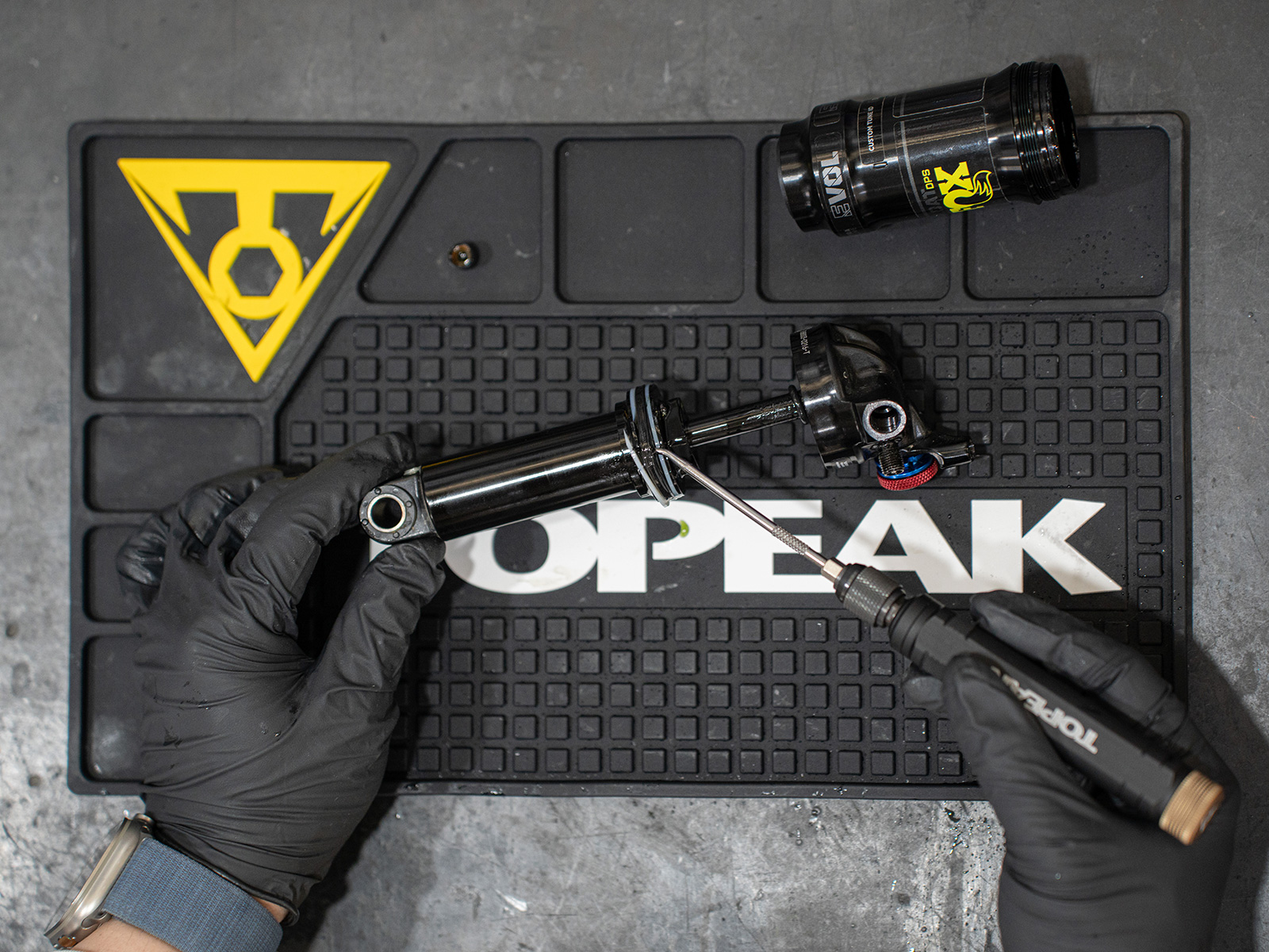 Tapis d'établi Topeak, en usage réel, des mains gantées tiennent un amortisseur sur le tapis