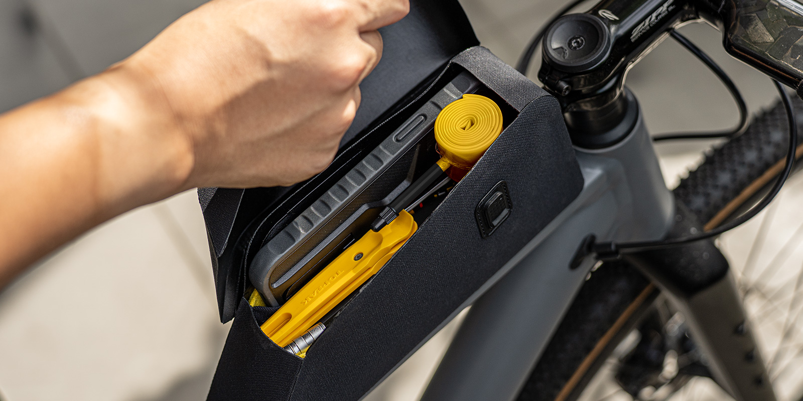 Geöffnete Topeak Toploader Dryshell Rahmentasche am Fahrrad, gefüllt mit Werkzeug, Ersatzschlauch und Smartphone.