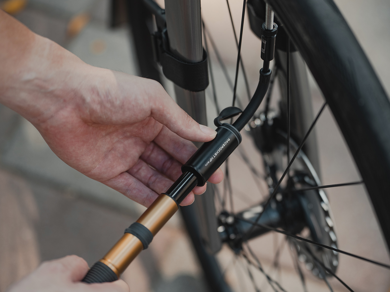 Topeak RaceRocket HP Mini Minipumpe in Schwarz/Gold beim Aufpumpen eines Fahrradreifens am Ventil.