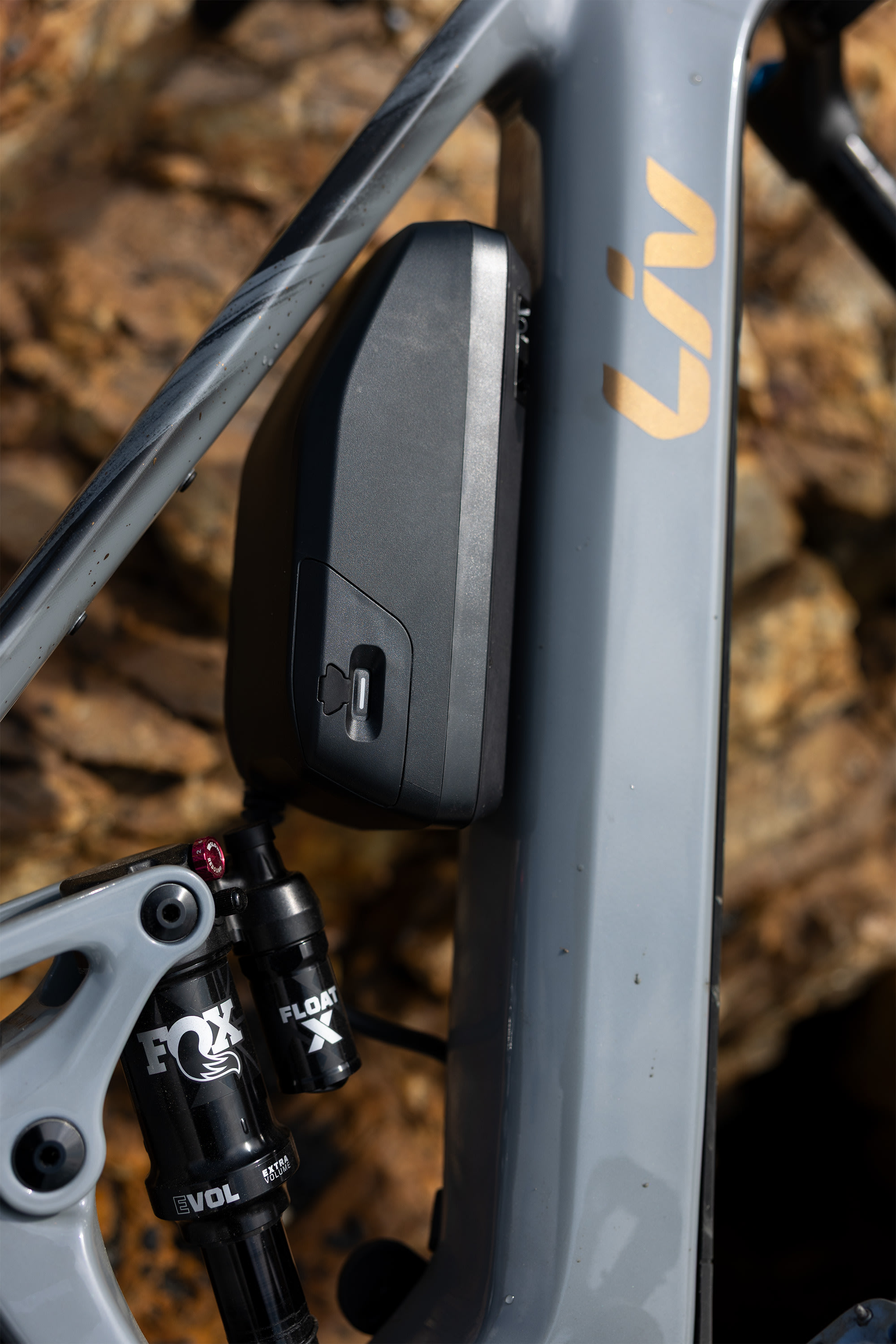 Liv Intrigue X Advanced E+ 1 E-Mountainbike in Stardust Grey mit externem Range Extender am Rahmen.