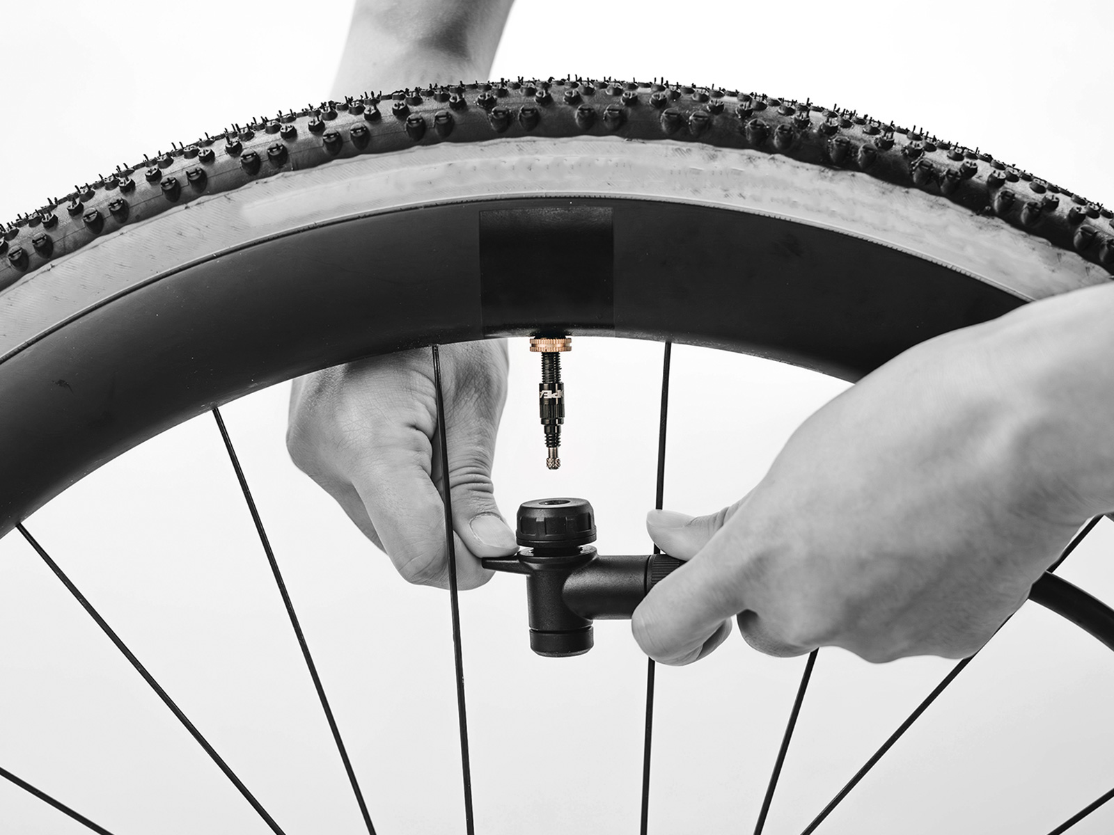  Schwarz-weiß-Foto von Händen, die einen RapidHead-Pumpenkopf an ein Tubeless-Ventil eines Gravelbike-Reifens anschließen.